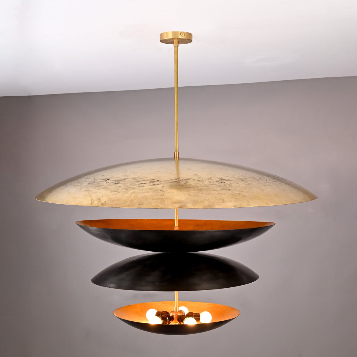 Front angle of illuminated 10-light layered disc chandelier with warm inner glow and contrasting black and gold brass bowls.