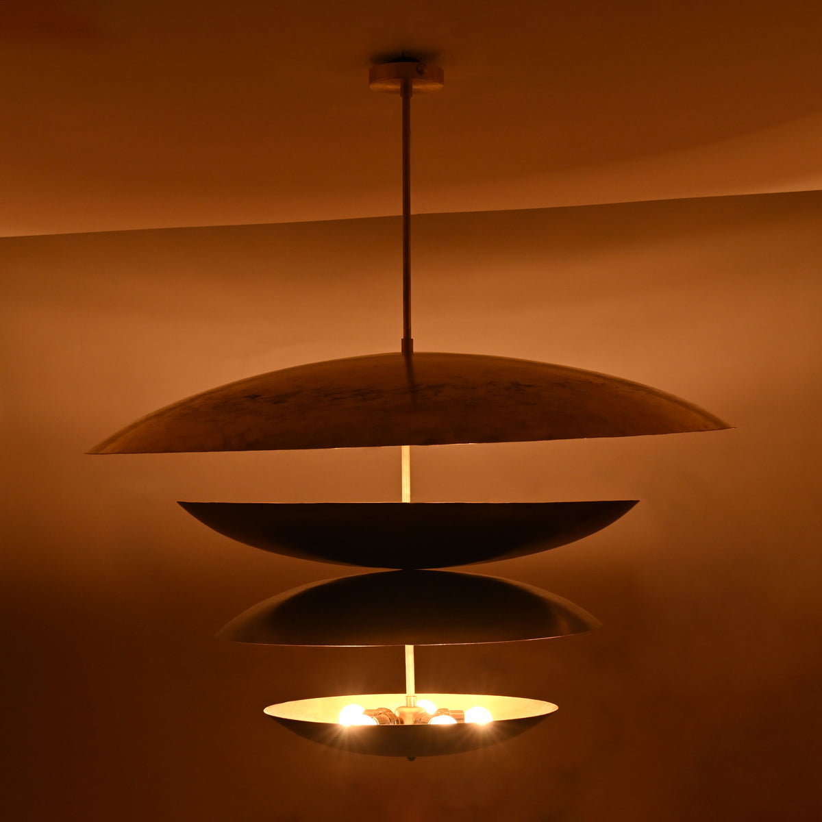 Warm night view of 10-light layered disc brass chandelier with sculptural stacked bowls glowing softly in ambient lighting.