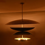 Warm night view of 10-light layered disc brass chandelier with sculptural stacked bowls glowing softly in ambient lighting.