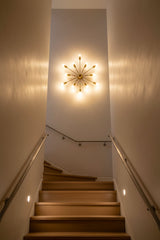 12-light brass wall sconce shown illuminated with warm glow and dramatic starburst lighting effect on the wall