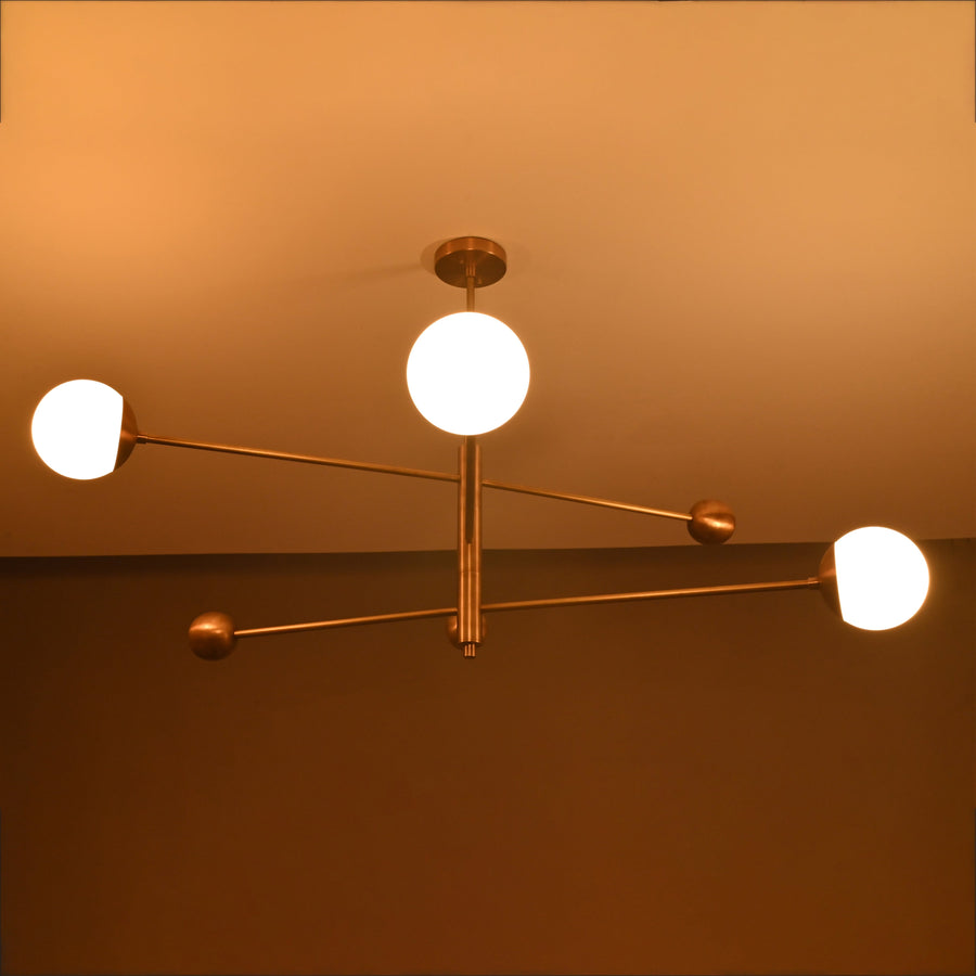 Handmade 3-light brass chandelier featuring balanced linear arms and frosted globes, mid-century modern ceiling fixture.
