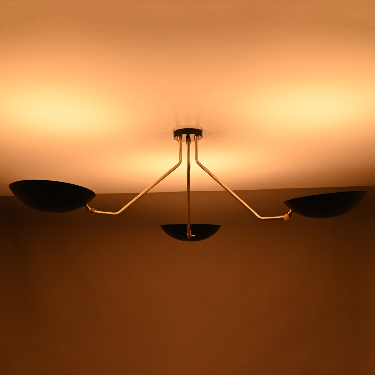 Three-light black and brass chandelier with warm upward glow and sculptural asymmetrical arms.