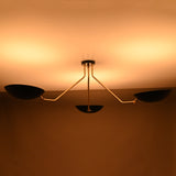 Three-light black and brass chandelier with warm upward glow and sculptural asymmetrical arms.