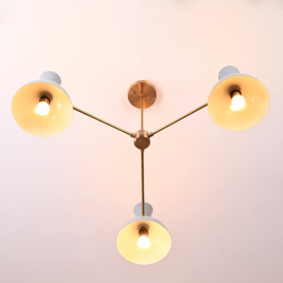 Bottom view of 3-light brass chandelier with white bowl-shaped shades and modern minimalist arms.