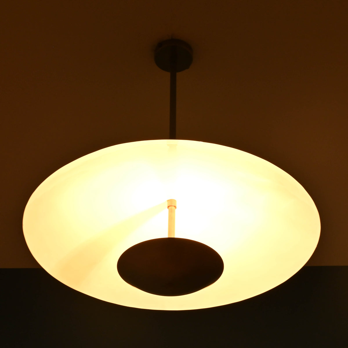 3 light disc style brass chandelier glowing softly with indirect light and sculptural brass design