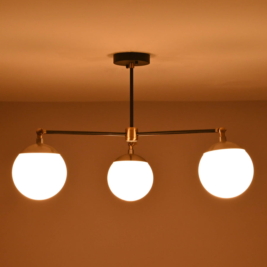 Front view of a 3 light opal glass globe brass chandelier with black arms and brushed brass accents.