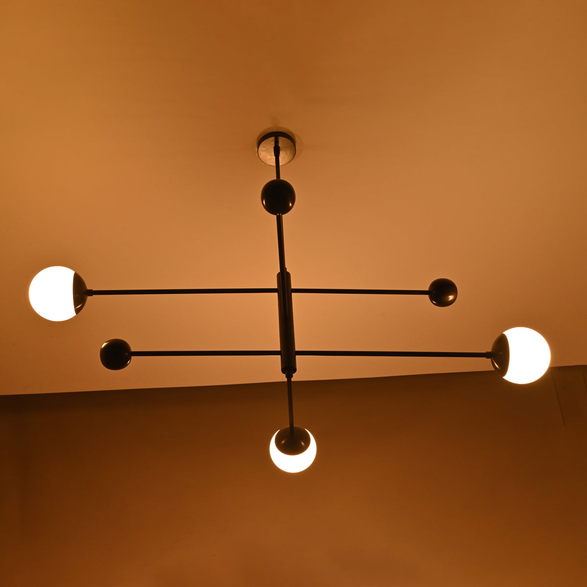 Matte black balance chandelier softly glowing in warm ambient light – diagonal angle