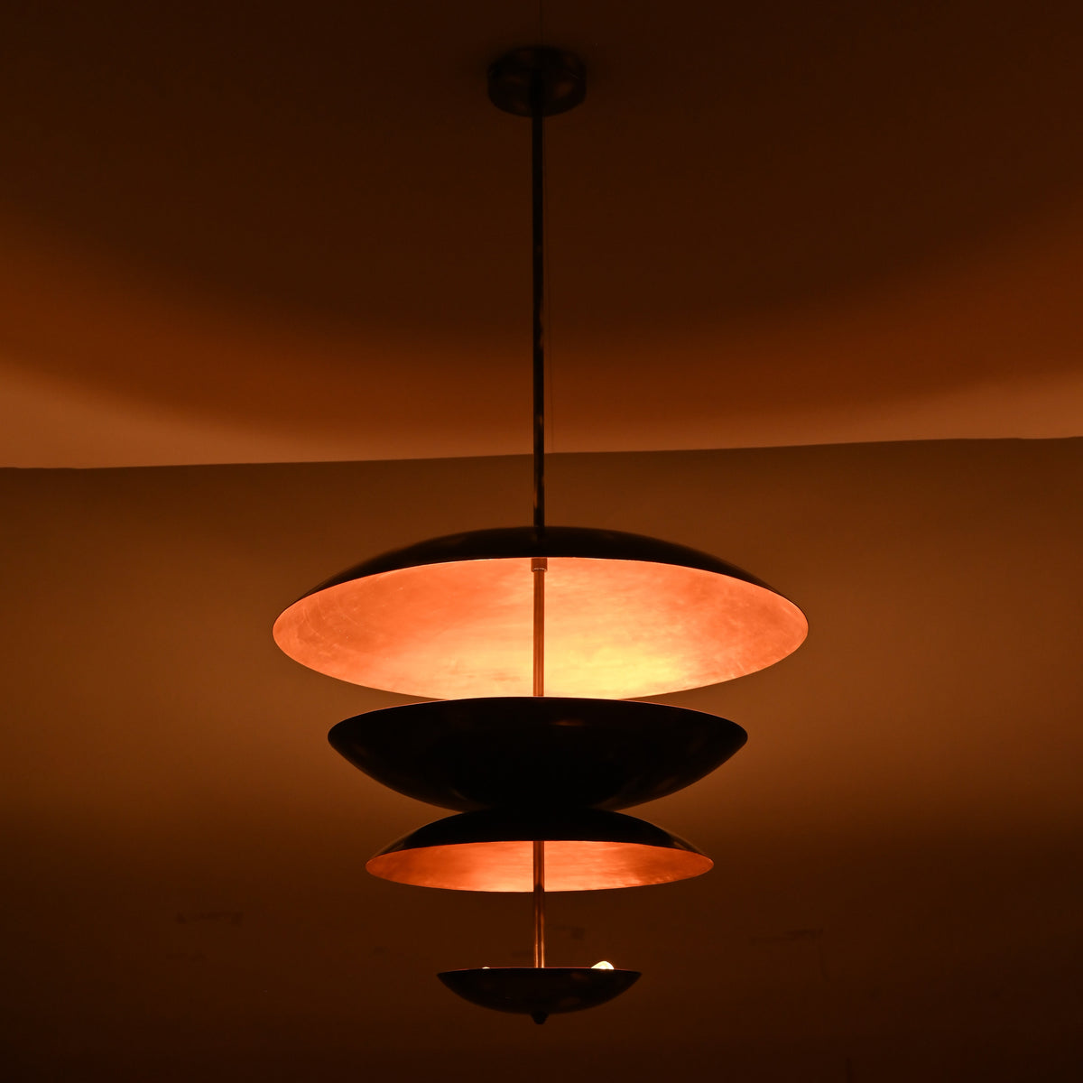 Blackened brass and copper layered pendant light glowing in low light