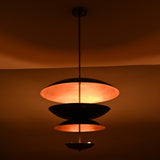 Blackened brass and copper layered pendant light glowing in low light