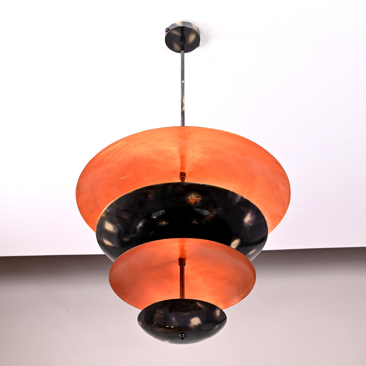 Large top bowl shade of blackened brass pendant showing copper interior glow