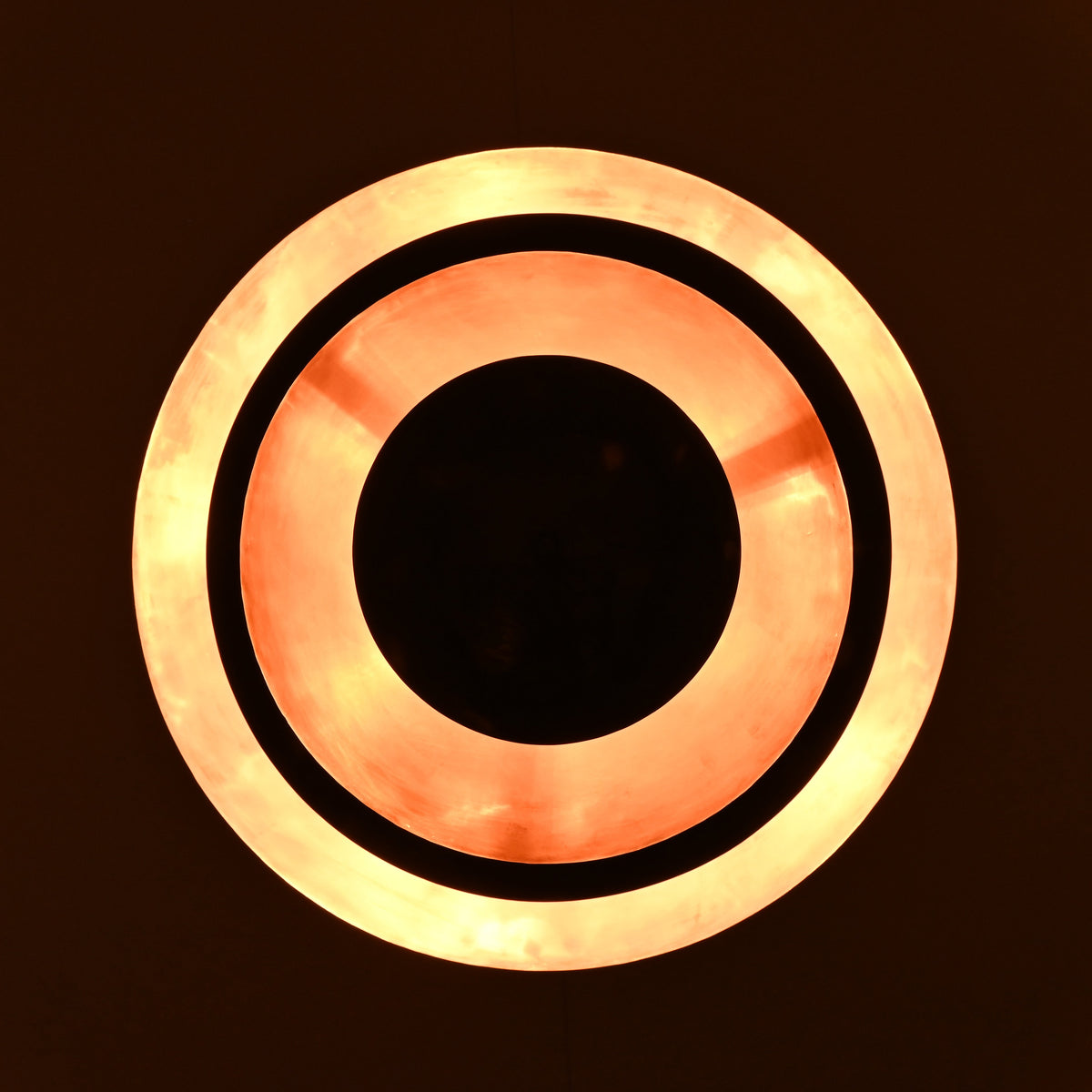 Illuminated blackened brass pendant light showing glowing copper interior