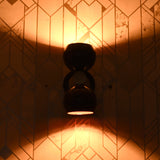 Burgundy double globe wall sconce lit up, casting warm ambient light upward and downward against patterned wall.
