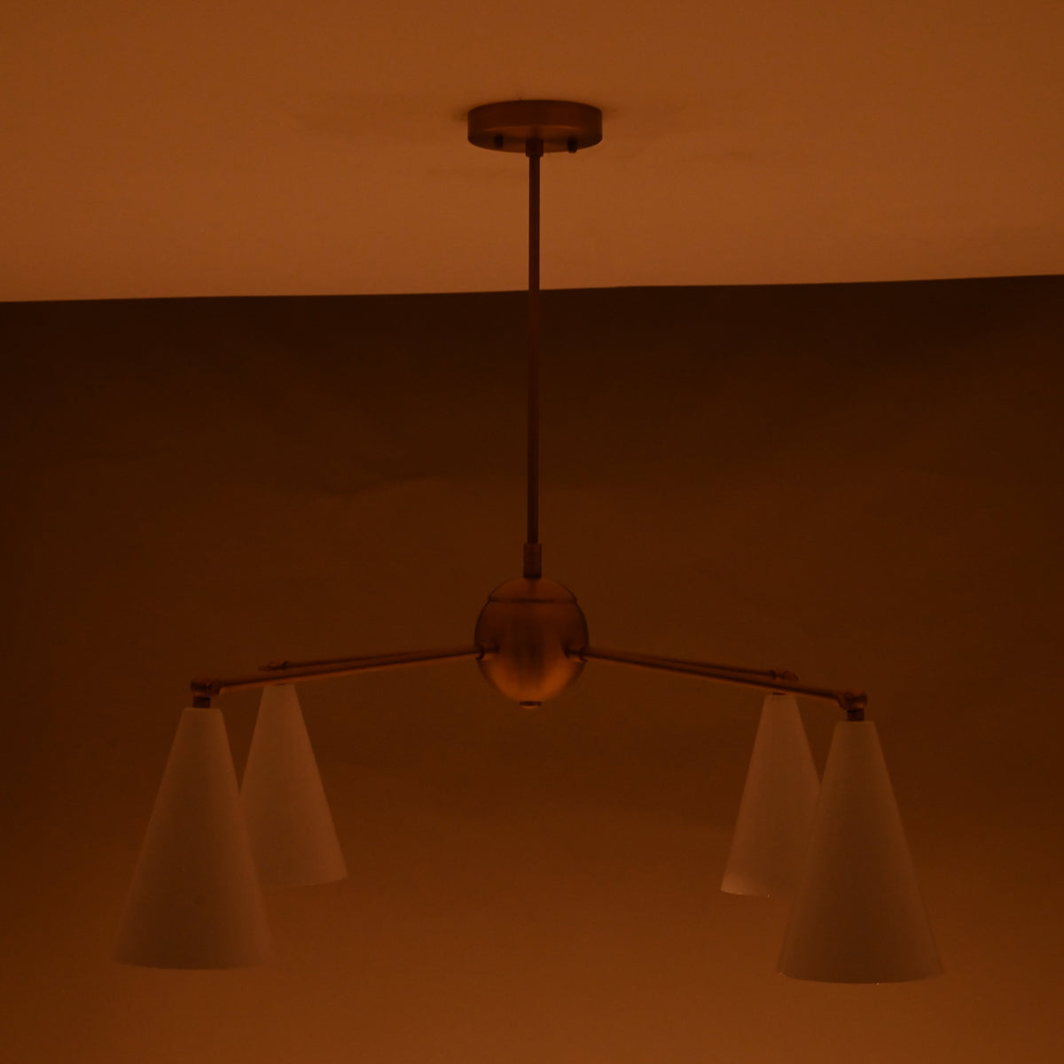 Warm-lit 4-light brass chandelier with white cone shades in a dimly lit room.