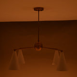 Warm-lit 4-light brass chandelier with white cone shades in a dimly lit room.