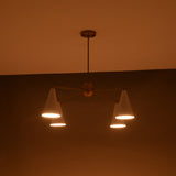 Illuminated brass chandelier with four downward-facing white cone shades, modern mid-century style.