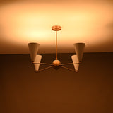 Brass ceiling chandelier glowing warmly with four white cone shades during nighttime.