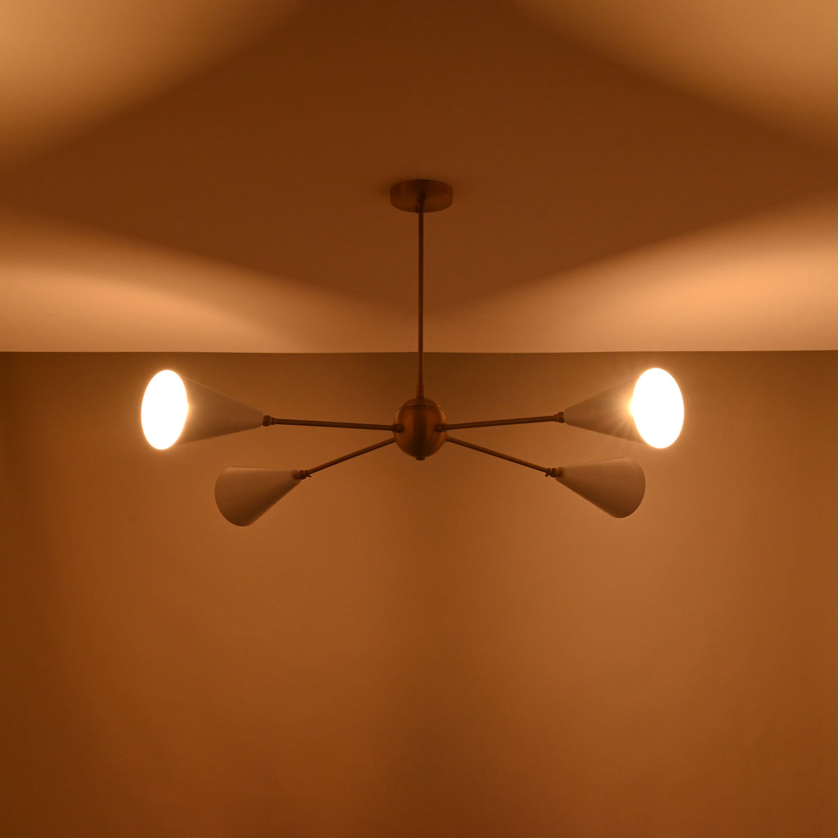 Warm-lit ceiling view of a 4-light brass chandelier with cone-shaped white shades