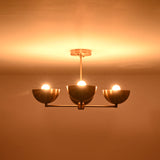 Front view of a 4 bowl brass chandelier in a dark setting, emphasizing warm light diffusion and the sculptural brass bowl shades.