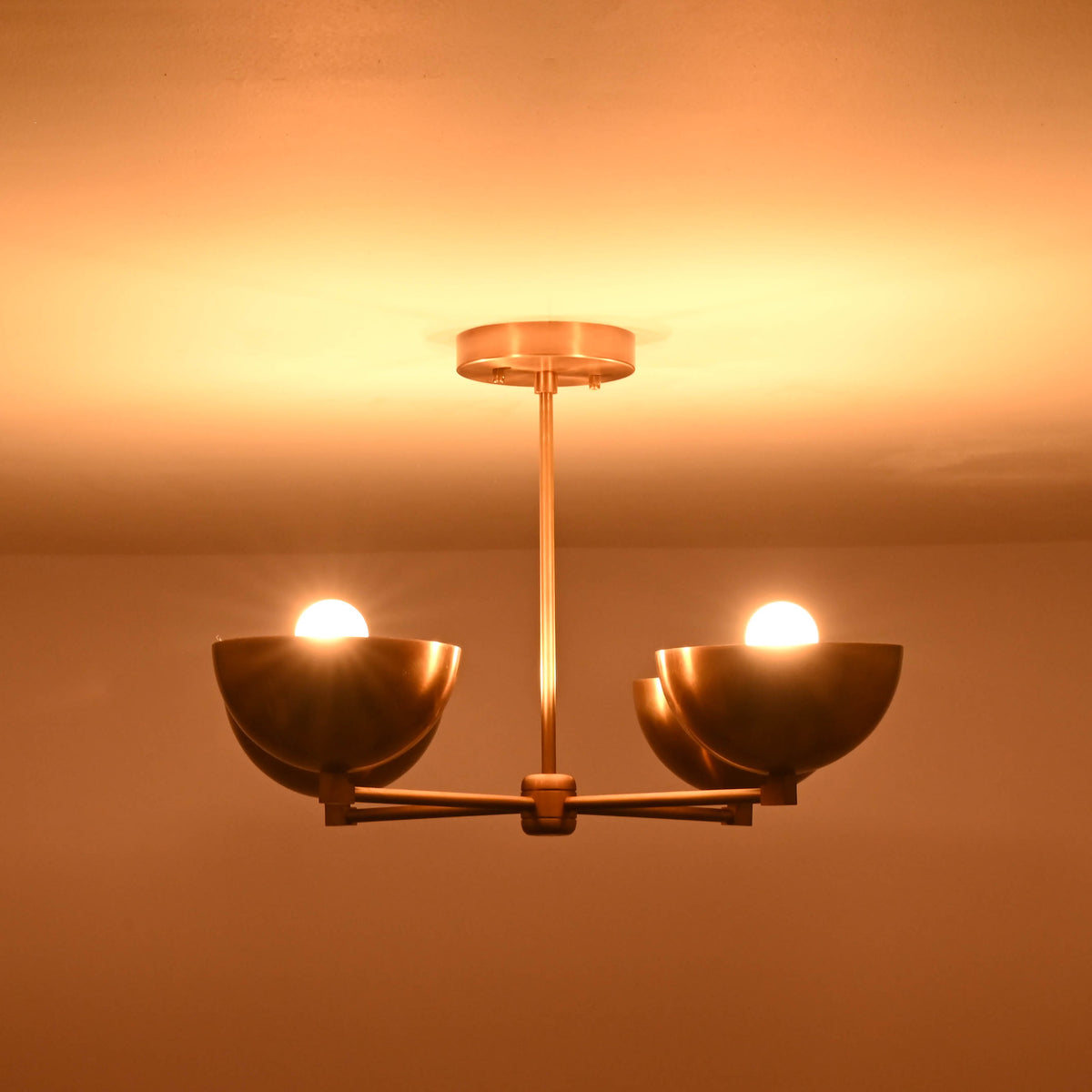 Side profile of a 4 bowl brass chandelier in low light, showcasing the balanced arm structure and warm reflective brass surface.