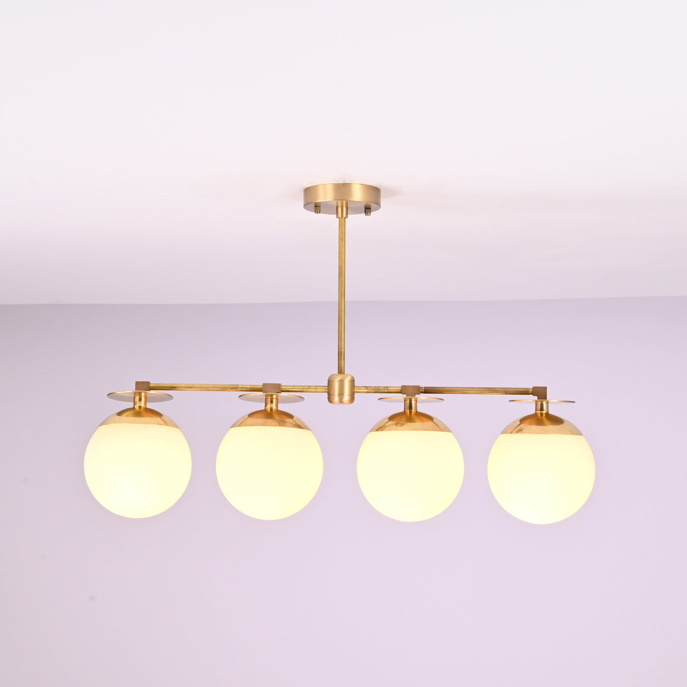 Front view of 4 linear brass chandelier with opal glass globe shades, showcasing minimalist industrial design and warm ambient lighting.