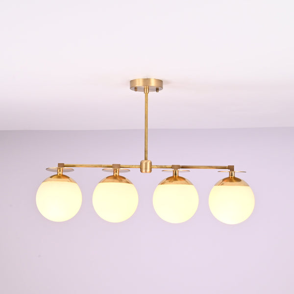 Front view of 4 linear brass chandelier with opal glass globe shades, showcasing minimalist industrial design and warm ambient lighting.