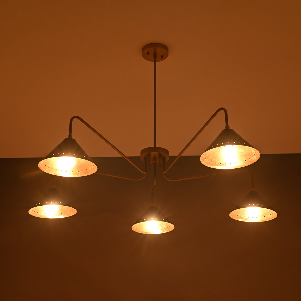 Warm-lit view of 5-light brass chandelier showing glowing cone shades creating soft ambient lighting.