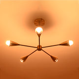 Lit view of handcrafted brass ceiling chandelier with five conical light arms, creating a golden modern glow in luxury interior spaces.