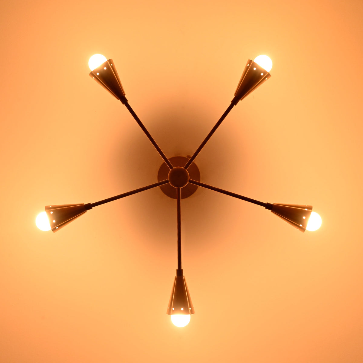 Illuminated 5-light brass cone chandelier casting warm ambient light with mid-century style elegance, ideal for refined home and commercial interiors.