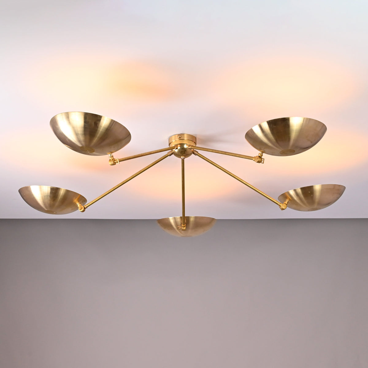 Angled view of handcrafted 5-light brass ceiling chandelier featuring bowl-shaped shades and minimalist arms.