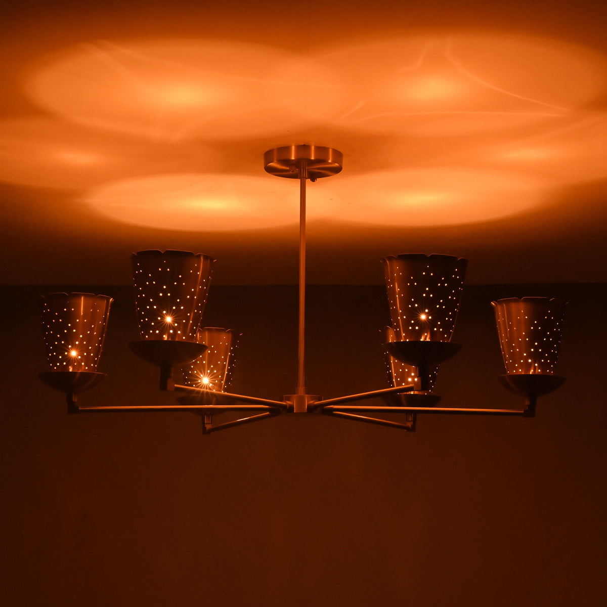Side view of 6 light brass cone shade chandelier illuminated with warm ambient glow, creating soft indirect uplighting.