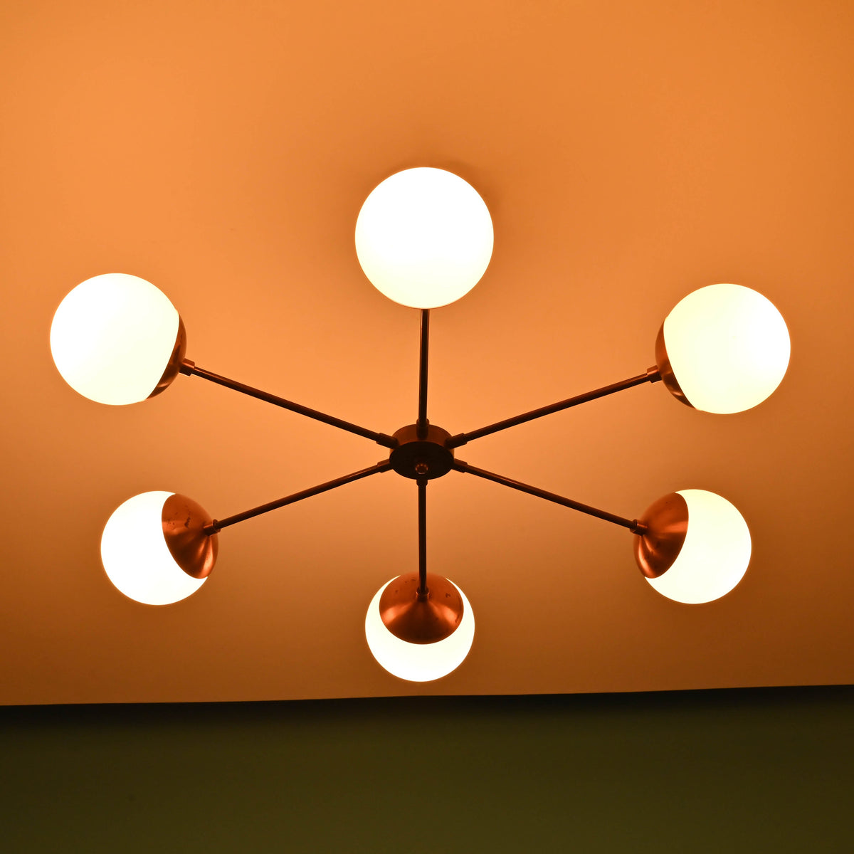Warm lit 6 light glass globe brass chandelier showcasing symmetrical mid-century design and handcrafted brass details