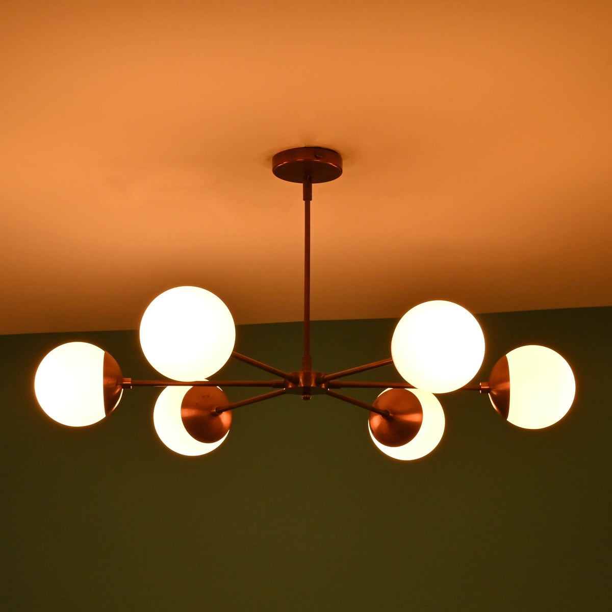 Angled night view of 6 light glass globe brass chandelier with glowing opal glass globes and elegant brass finish