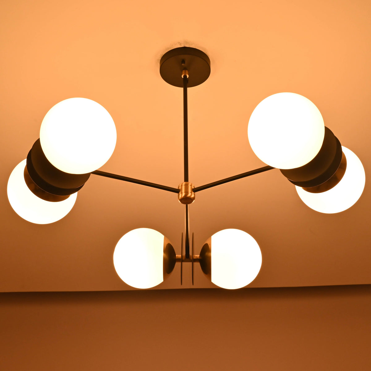 Warm-lit symmetrical view of a handcrafted opal glass globe brass chandelier suspended from the ceiling.