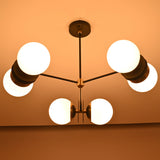 Warm-lit symmetrical view of a handcrafted opal glass globe brass chandelier suspended from the ceiling.