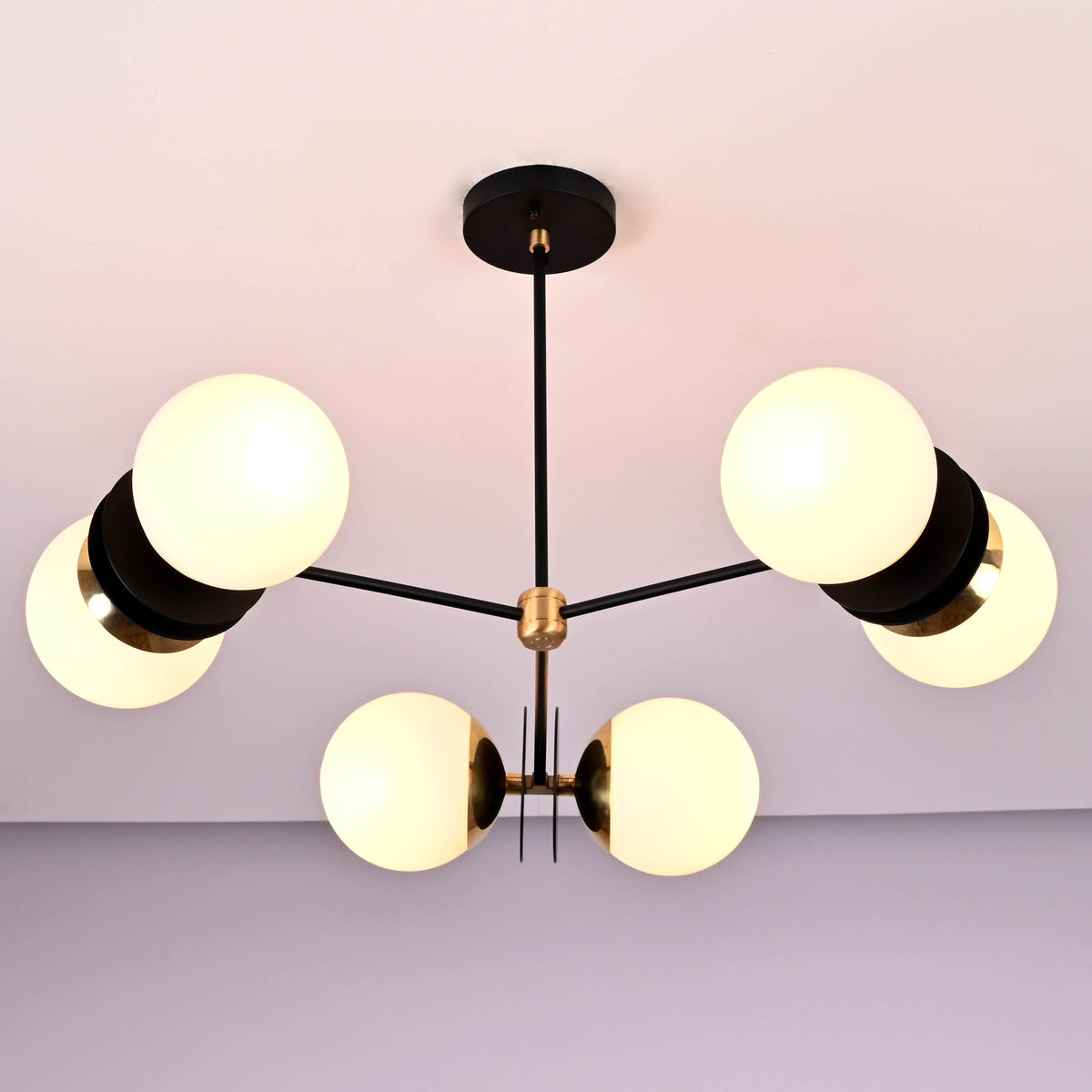 Symmetrical view of a handcrafted brass chandelier with six opal glass globes and minimalist industrial styling.