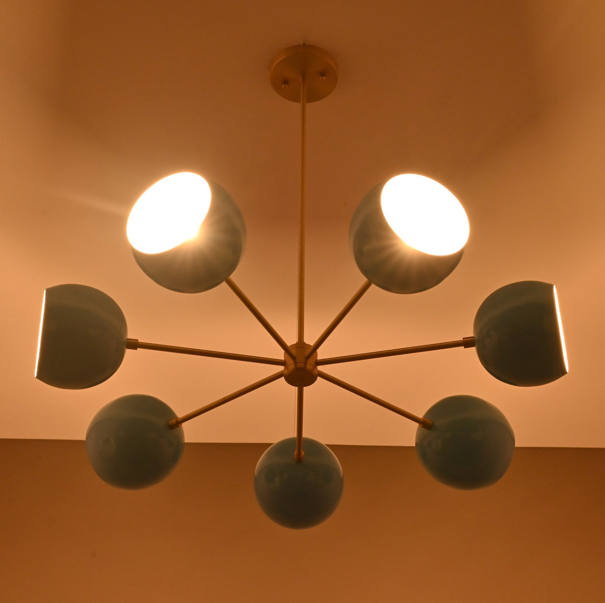 Installed 7 bowl brass chandelier emitting warm ambient light with blue glass shades