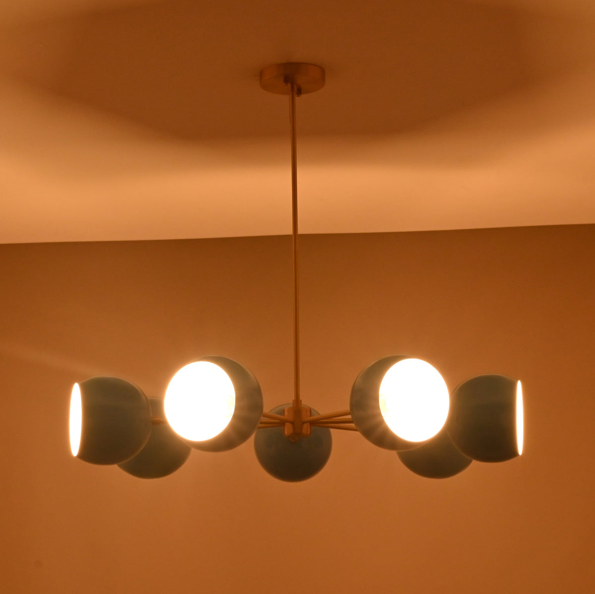 Symmetrical 7 bowl brass chandelier with blue glass shades installed in contemporary space