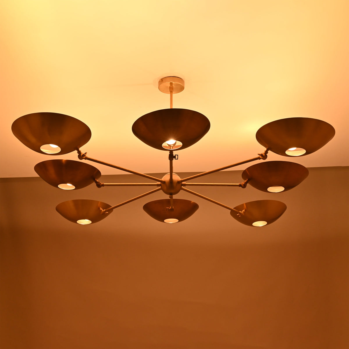 Side view of modern brass disc chandelier casting warm ambient lighting across the ceiling.
