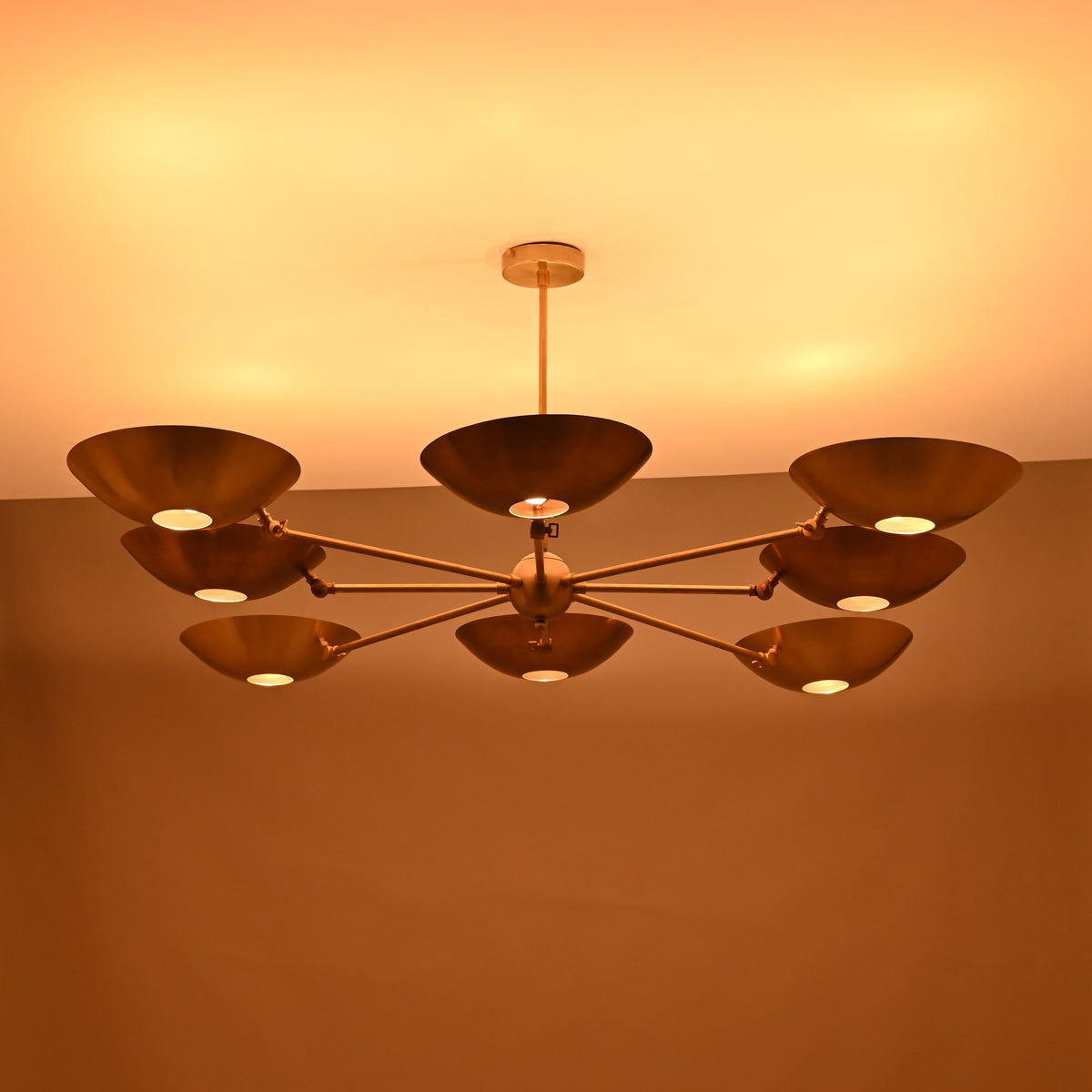 Evening-lit brass disc chandelier with eight disc shades emitting soft warm light in a symmetrical layout.