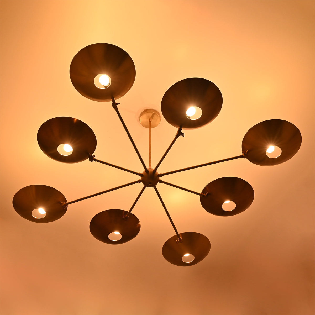 Warm-lit brass disc chandelier with eight glowing bulbs and circular concave brass shades.
