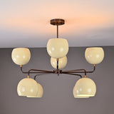 Minimalist 8-light brass ceiling light with curved arms and cream bowl shades, photographed in warm ambient mode.