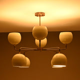 Side angle of warm-lit 8-light chandelier with ivory glass bowl shades and industrial brass frame.