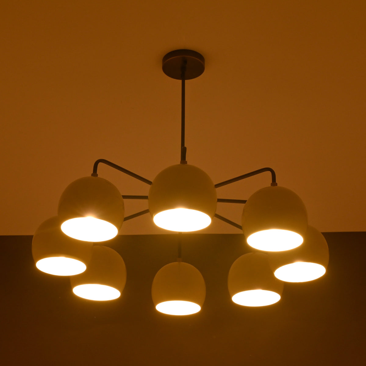 8-light brass chandelier glowing with warm ambient lighting, featuring dome-shaped shades and minimalist arms.
