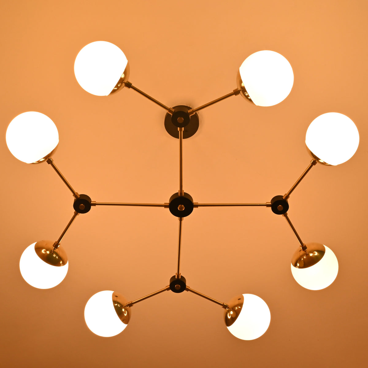 8-light brass globe chandelier illuminated with warm ambient lighting, showcasing opal glass shades and modern linear form.