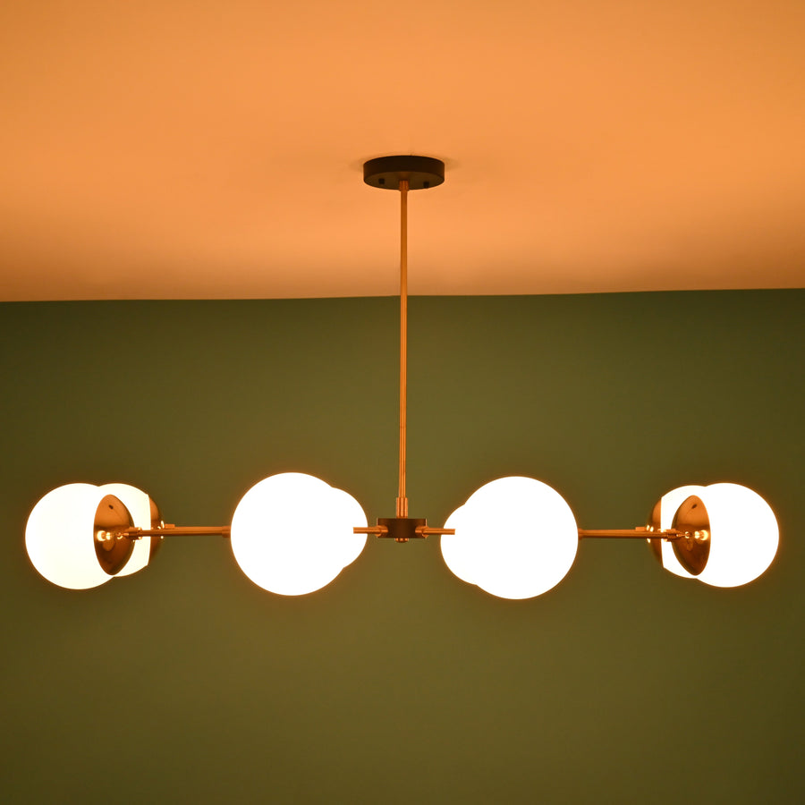 Front view of an 8-light brass globe linear sputnik chandelier with opal glass shades and black accents, suspended from the ceiling in a modern interior.