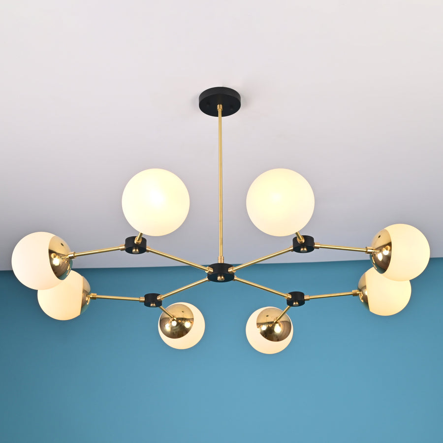 Front view of an 8-light brass globe linear sputnik chandelier with opal glass shades and black accents, suspended from the ceiling in a modern interior.