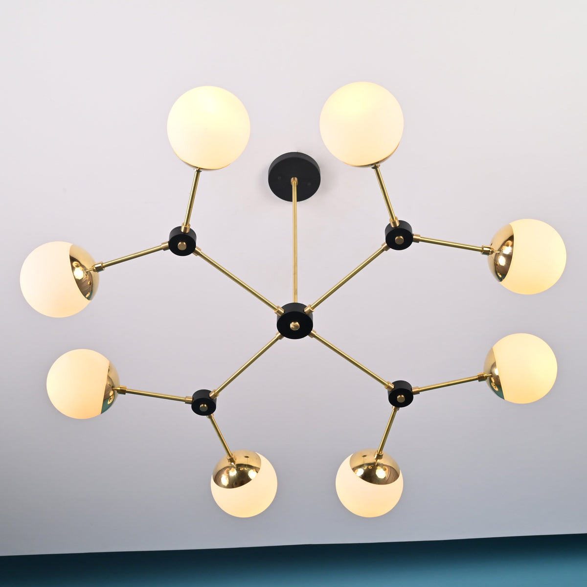 Angled view of an 8-light brass linear chandelier with opal globe shades and black joint details, highlighting its balanced modern design.