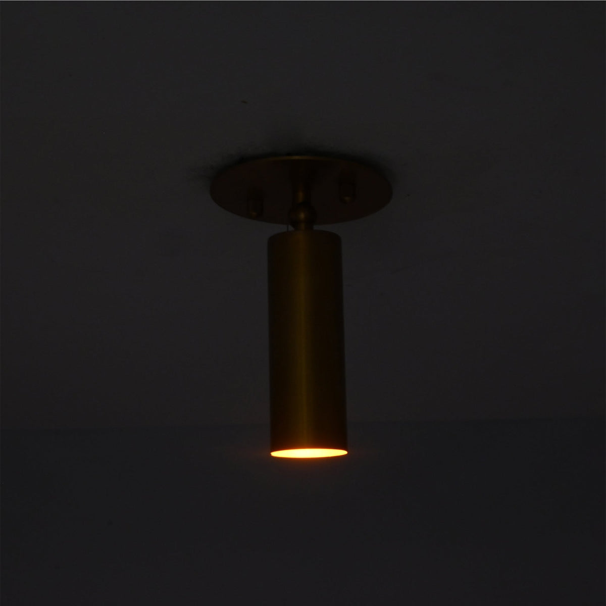 Lit view of Alden adjustable brass ceiling spotlight casting a warm focused downward beam
