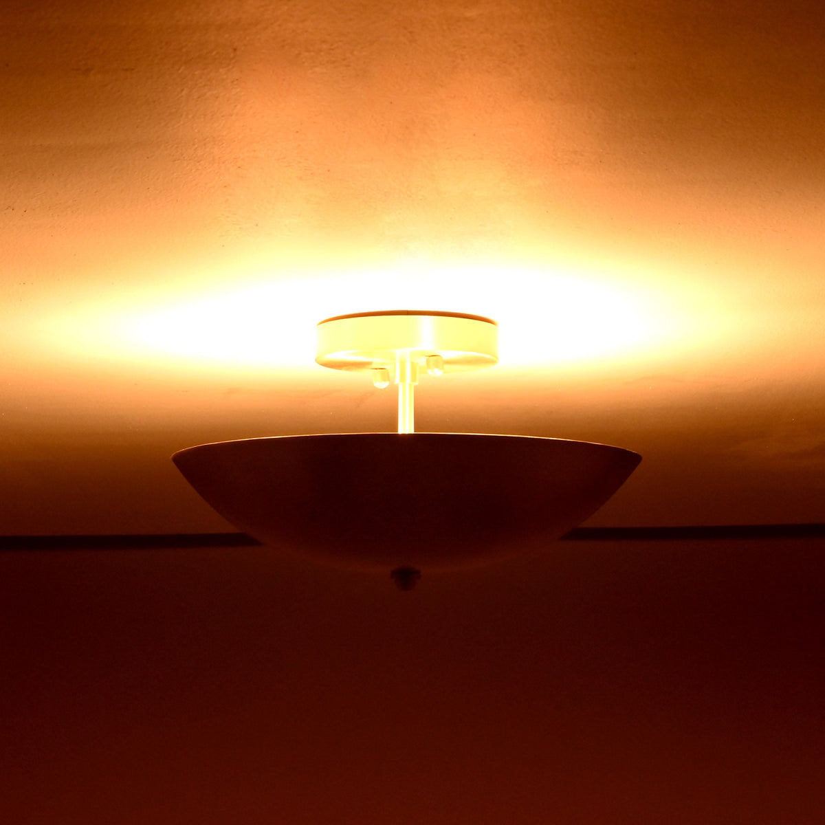 Brass bowl flushmount ceiling fixture radiating rich amber light across ceiling surface