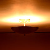 Brass bowl flushmount ceiling fixture radiating rich amber light across ceiling surface
